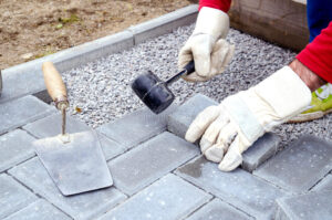 bricklayer-places-concrete-paving-stone-blocks-building-up-patio-using-hammer-58650246